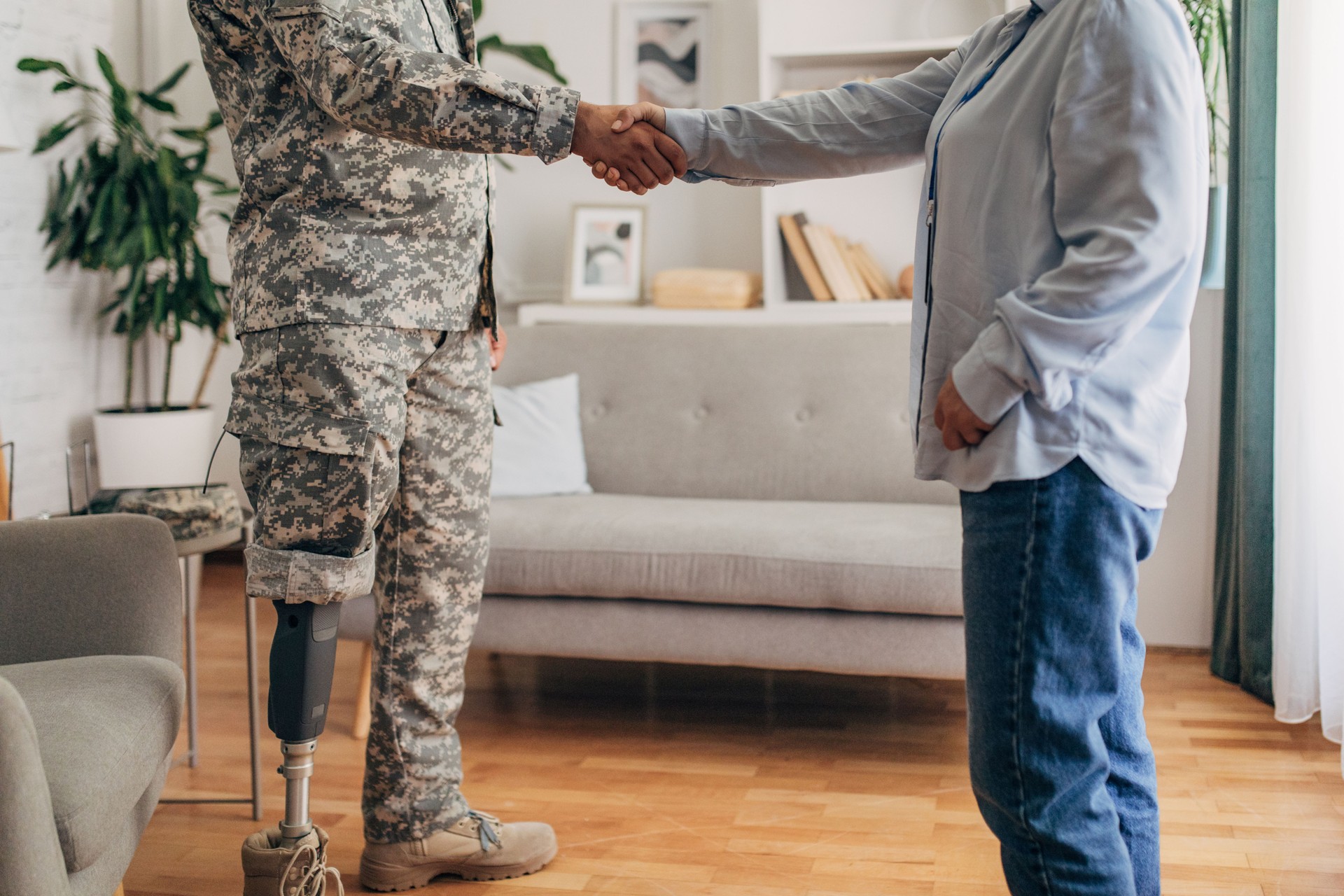 Veteran with a prosthetic leg and counselor shake hands in room with seating